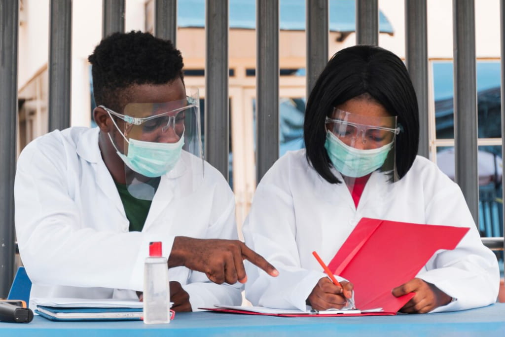 man and woman in masks reviewing documents in a red folder at an outdoor table